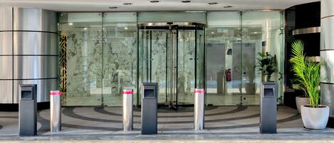 A modern hotel entrance with a revolving door, glass doors, and a security kiosk.