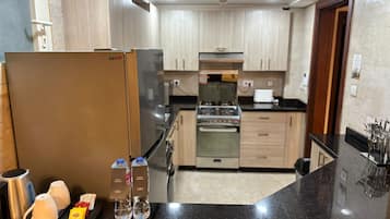 A modern kitchen with a refrigerator, stove, and microwave. There are two bottles of water and a tray with a kettle, cups, and condiments.