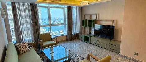 Una sala de estar moderna con sofá, mesa de centro y sillones, televisor de pantalla plana y vistas a la ciudad a través de amplias ventanas.
