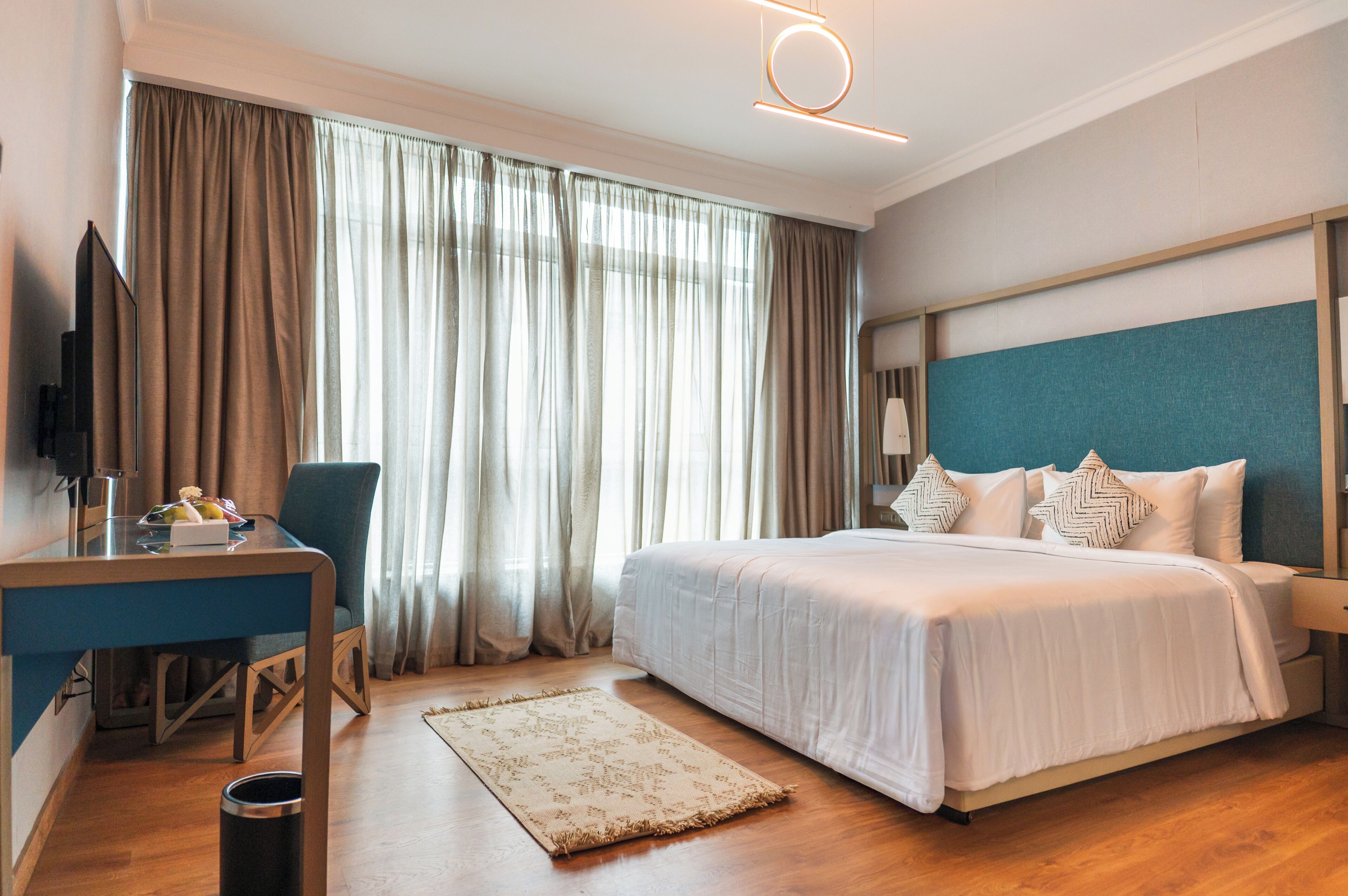 A hotel room with a bed, a desk, a chair, a TV, and a large window with curtains.