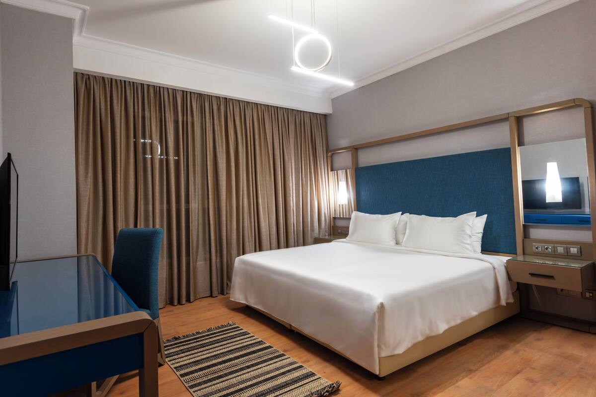 A hotel room with a large bed, a desk, a chair, a TV, and a mirror.