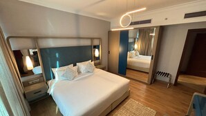 Una habitación de hotel moderna con una cama grande, mesitas de noche, un espejo y un pequeño rincón de descanso.
