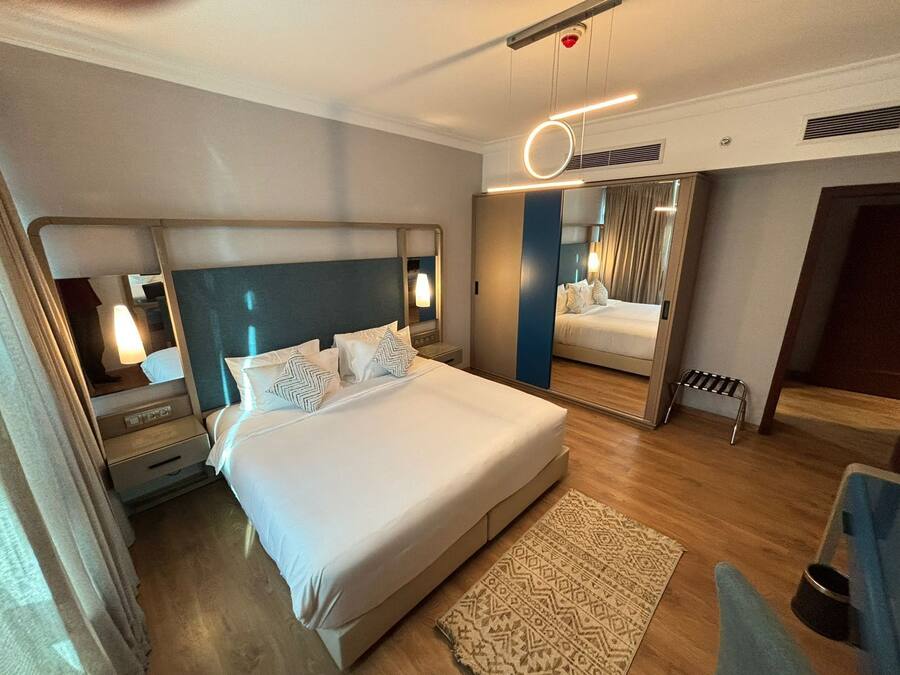 Een moderne hotelkamer met een groot bed, nachtkastjes, een spiegel en een klein zithoekje.