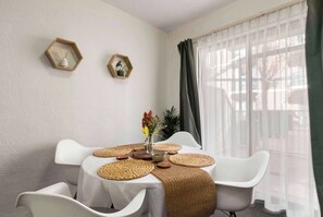 A dining area with a table set for four, white chairs, woven placemats, and a vase with flowers.
