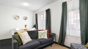 Una sala de estar moderna con un sofá gris, una mesita con una planta y una ventana con cortinas traslúcidas.