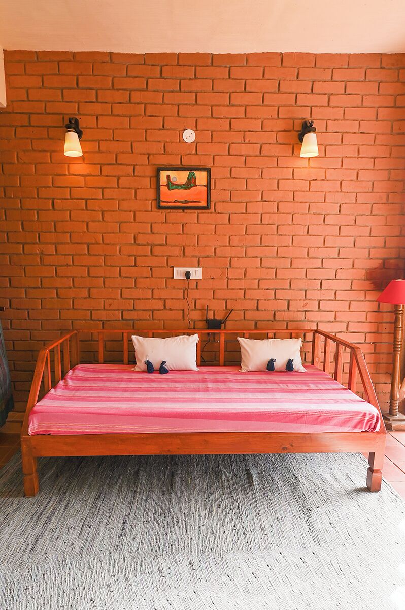A room with a brick wall, a wooden bed with a pink bedspread, two wall-mounted lamps, and a small picture frame.