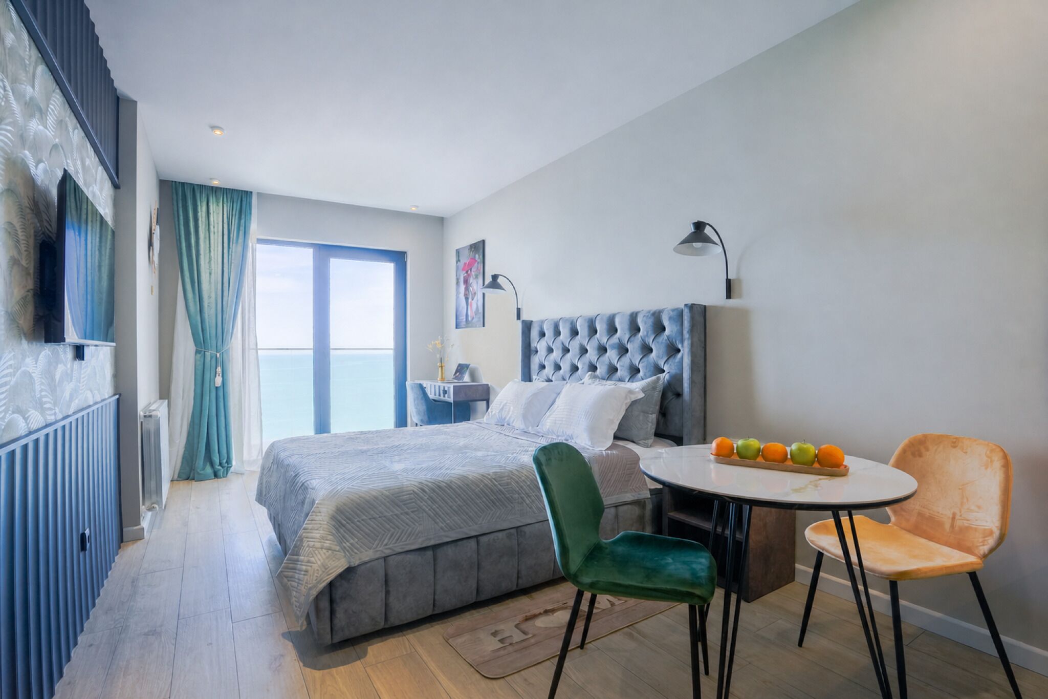 A hotel room with a bed, a dining table with chairs, a window with curtains, and a wall-mounted lamp.