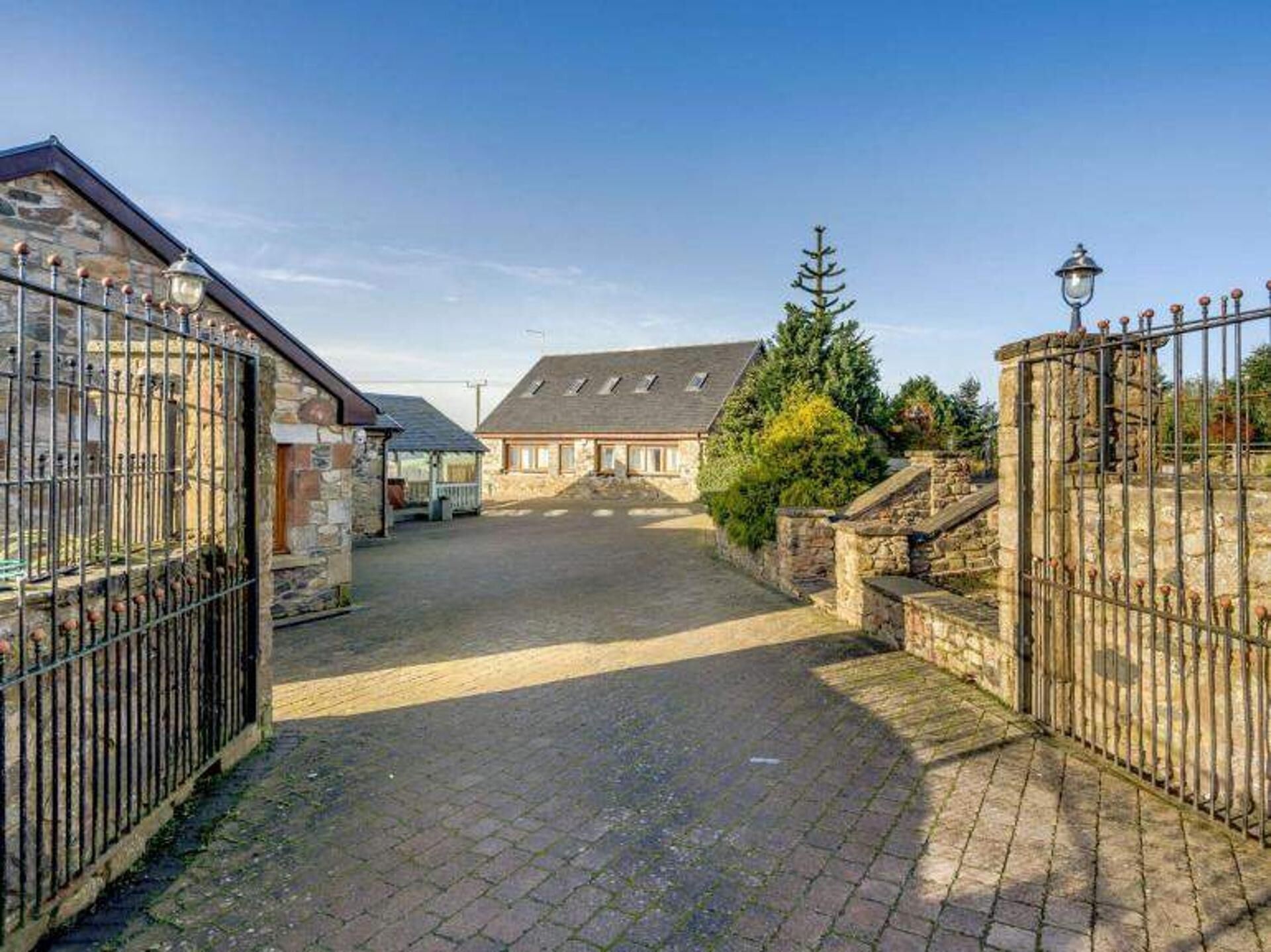 A stone building with a paved courtyard, a metal gate, and a lamp post.