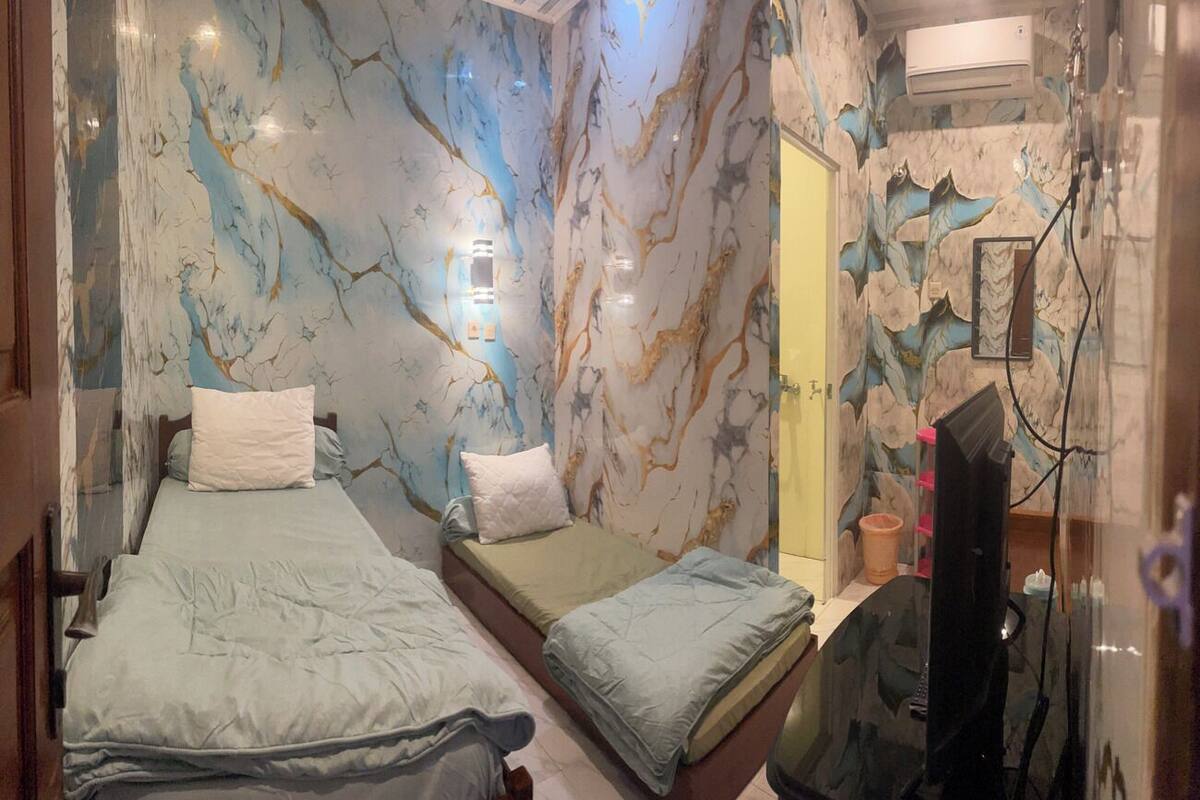 A room with two beds, marble-patterned walls, a small window, and a TV.