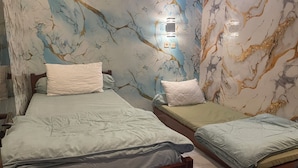 Two beds with white and green bedding, a marble-patterned wall, and a small window with a light fixture.