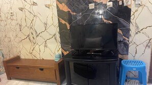 A room with a black entertainment unit, a wooden cabinet, and a blue stool.