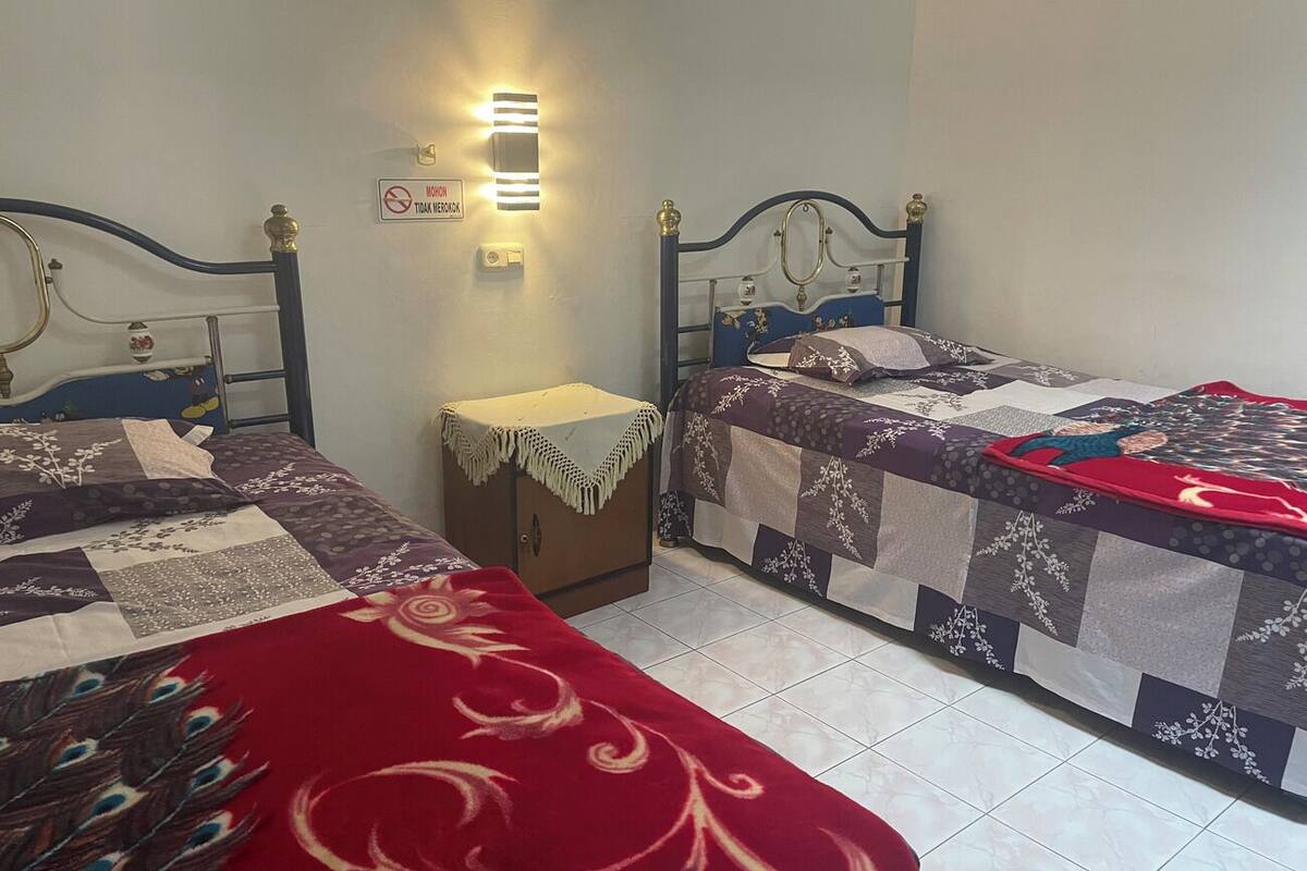 A bedroom with two single beds, a nightstand, a wall-mounted light, and a sign indicating no smoking.