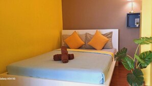 Ein ordentlich bezogenes Bett mit blauer Bettdecke und zwei orangefarbenen Kissen, ein braunes Handtuch und eine Nachttischlampe.