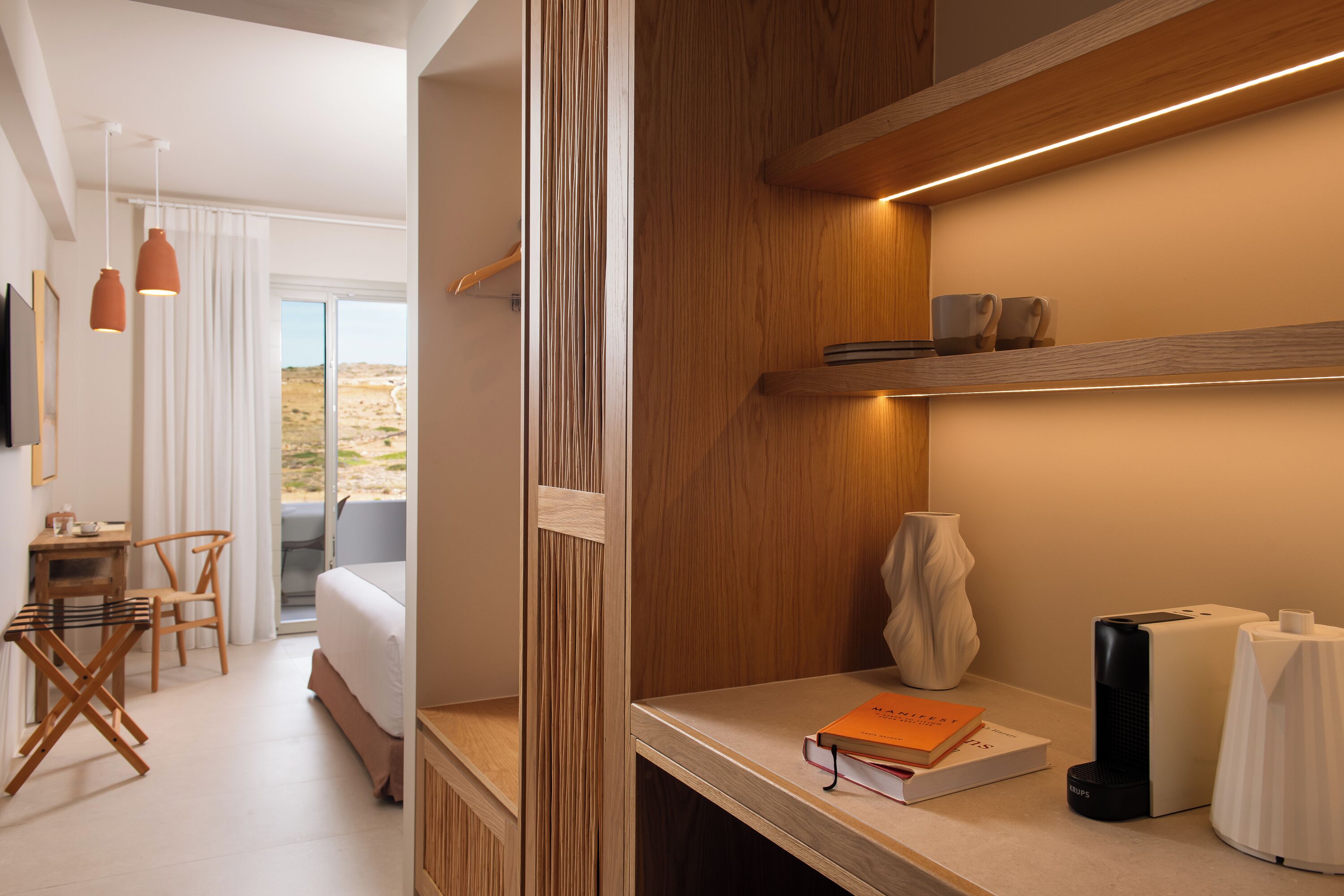 Una habitación de hotel moderna con cama, escritorio, silla, estantería y vistas al exterior.