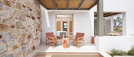 A modern outdoor seating area with stone walls, a wooden pergola, and a view of the interior.