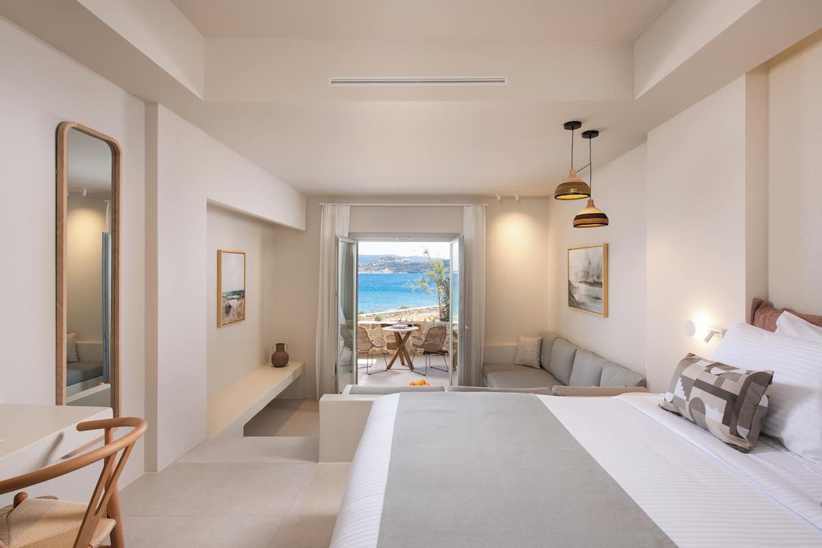 A modern hotel room with a large bed, a seating area with a view of the beach, and a dining table.
