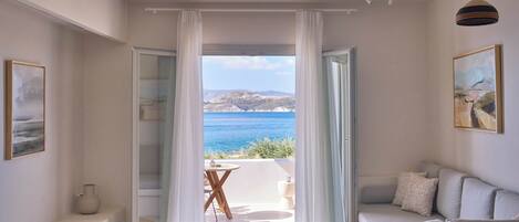 Un dormitorio con vistas al mar, un balcón con mesa y sillas, y un sofá con cojines.
