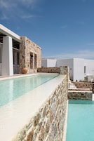 Zona de piscina con muros de piedra y un cielo azul despejado.