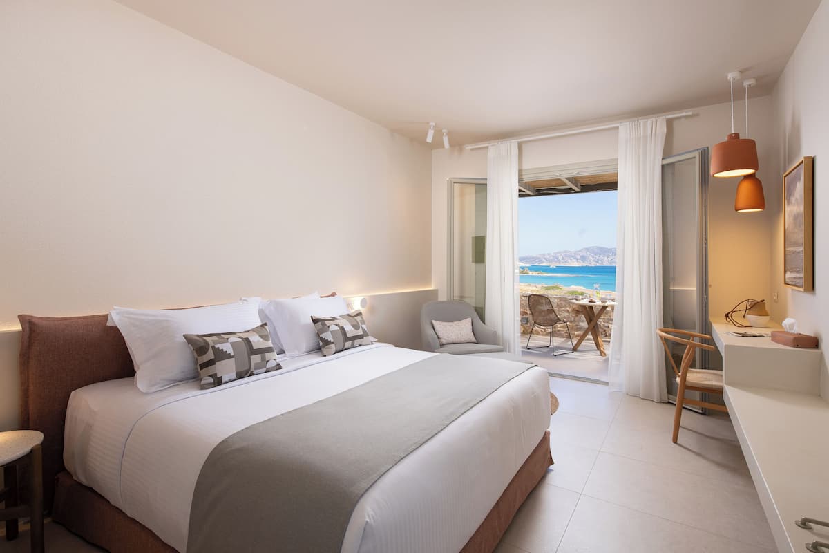 A bedroom with a large bed, a desk, and a view of the beach.
