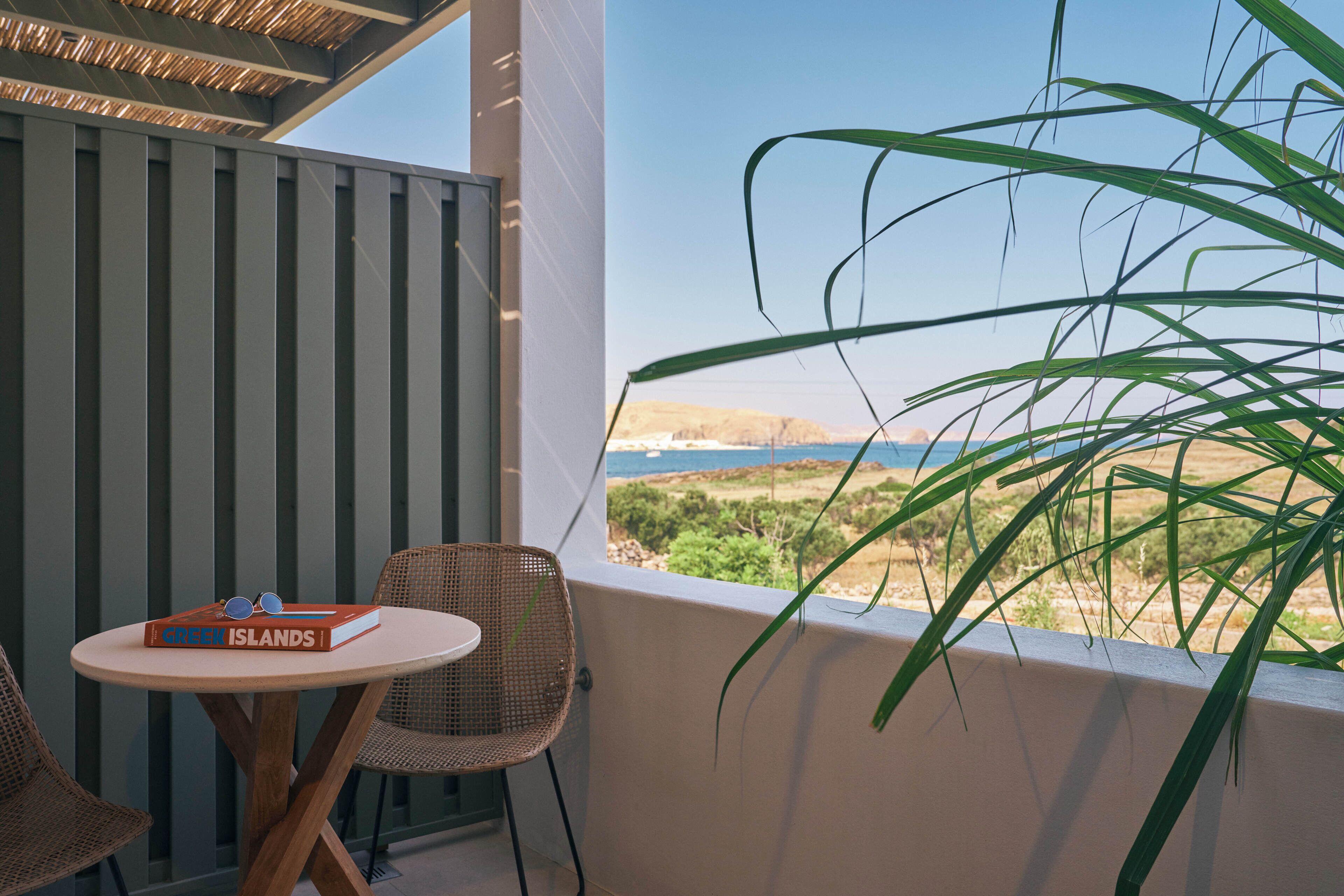 A balcony with a view of the sea, a table with a book and sunglasses, and wicker chairs.
