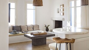 A modern living room with a large window, a fireplace, a round coffee table, and a seating area with cushions.