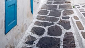 A narrow, cobblestone street flanked by white buildings with blue doors and shutters.