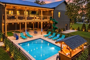 A two-story house with a swimming pool, outdoor seating, and a slide.