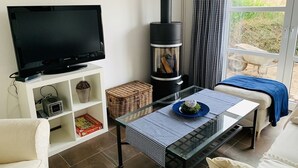 A living room with a TV, a glass table, a sofa, and a wood-burning stove.