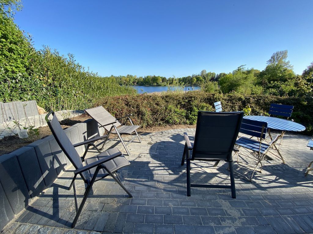 Un patio al aire libre con sillas y una mesa, con vista a una masa de agua y follaje.