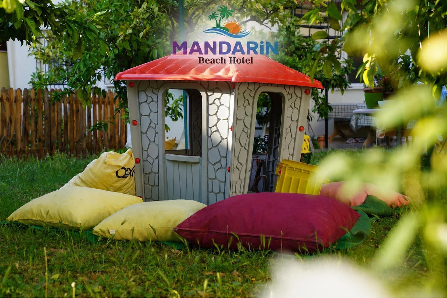 Une petite construction à un seul étage, avec un toit rouge, portant l’inscription « Hôtel Mandarin Beach », entourée de pelouse et d’une clôture en bois.