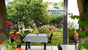 A patio area with a table and chairs, surrounded by greenery and a sign for Mandarin Beach Hotel. - Mandarin Beach Hotel ve Restaurant  (Menderes)