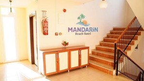 A hotel lobby with a staircase, a fire extinguisher, a cabinet, and a wall-mounted sign for Mandarin Beach Hotel. - Mandarin Beach Hotel ve Restaurant  (Menderes)