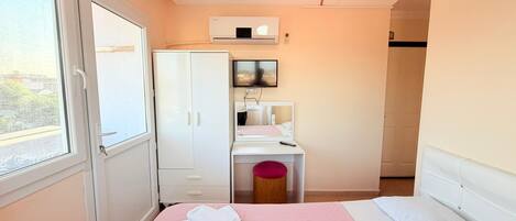 Un dormitorio con cama, armario, escritorio con espejo y ventana.