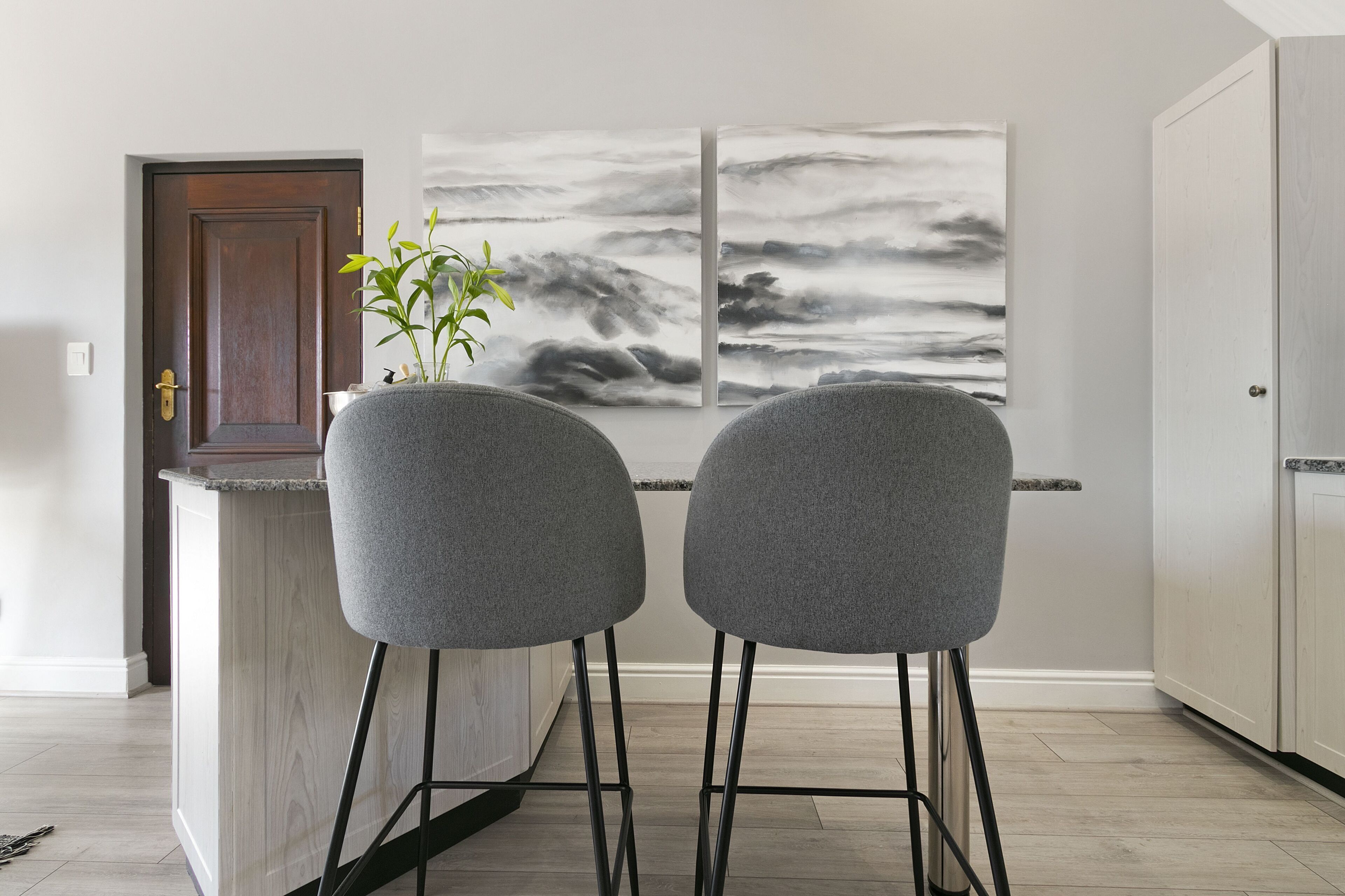 A kitchen with two grey bar stools, a wooden door, and two abstract paintings on the wall.