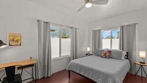 A bedroom with a bed, two bedside tables with lamps, a desk with a chair, and a ceiling fan.