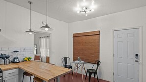 A compact kitchen with a wooden table, two chairs, a small round table with a decorative item, and a white door.