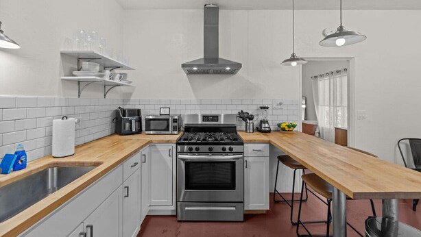 A modern kitchen with white cabinets, stainless steel appliances, a wooden countertop, and pendant lighting.
