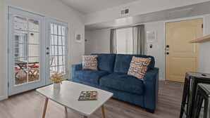 Una sala de estar moderna con un sofá azul, una mesa de centro blanca y una puerta que da a un espacio exterior.
