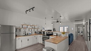 Una cocina moderna con armarios blancos, electrodomésticos de acero inoxidable y encimeras de madera. Cuenta con una isla central con fregadero e iluminación empotrada.