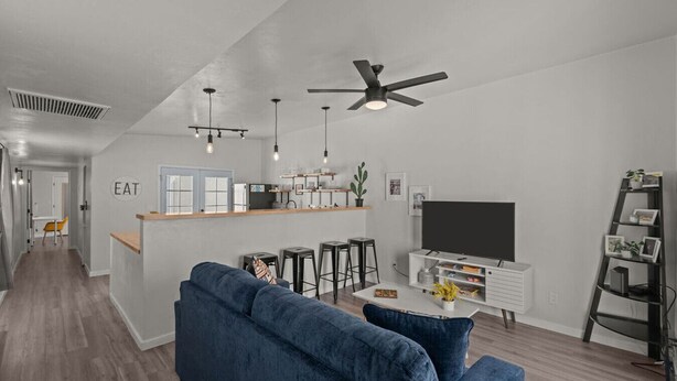 Una sala de estar moderna con un sofá azul, televisión y una zona de cocina con barra.