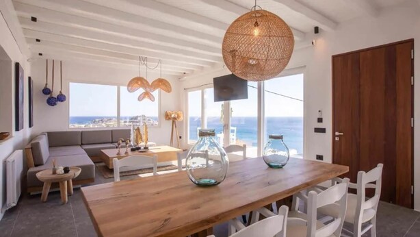 A modern dining area with a wooden table, white chairs, and a large woven pendant light. - My Rental Homes - Villa Waves with pool and Jacuzzi. Close to Platis Gialos beach (Mykonos)