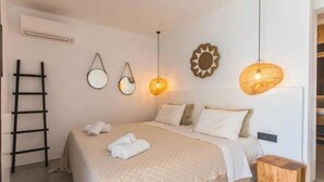 A bedroom with a bed, two wall-mounted mirrors, a ladder, and a wooden stool. - My Rental Homes - Villa Waves with pool and Jacuzzi. Close to Platis Gialos beach (Mykonos)