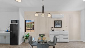 Una cocina moderna con comedor, que incluye una mesa de vidrio, sillas grises, un refrigerador negro, un microondas y un armario blanco.