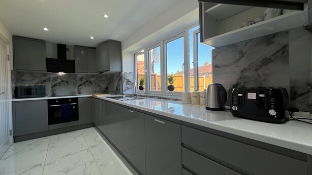 A modern kitchen with a marble backsplash, a built-in oven, and a coffee maker on the counter. - Perfect Contractor house/3 free parking space/EV charging/Secure/Quiet/Modern (Waltham Cross)