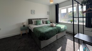 A modern bedroom with a large bed, two bedside tables, a window with a view, and a hanging light fixture. - Perfect Contractor house/3 free parking space/EV charging/Secure/Quiet/Modern (Waltham Cross)