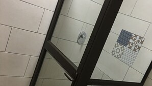 En dusch med glasväggar, kaklat golv och en svart ram.