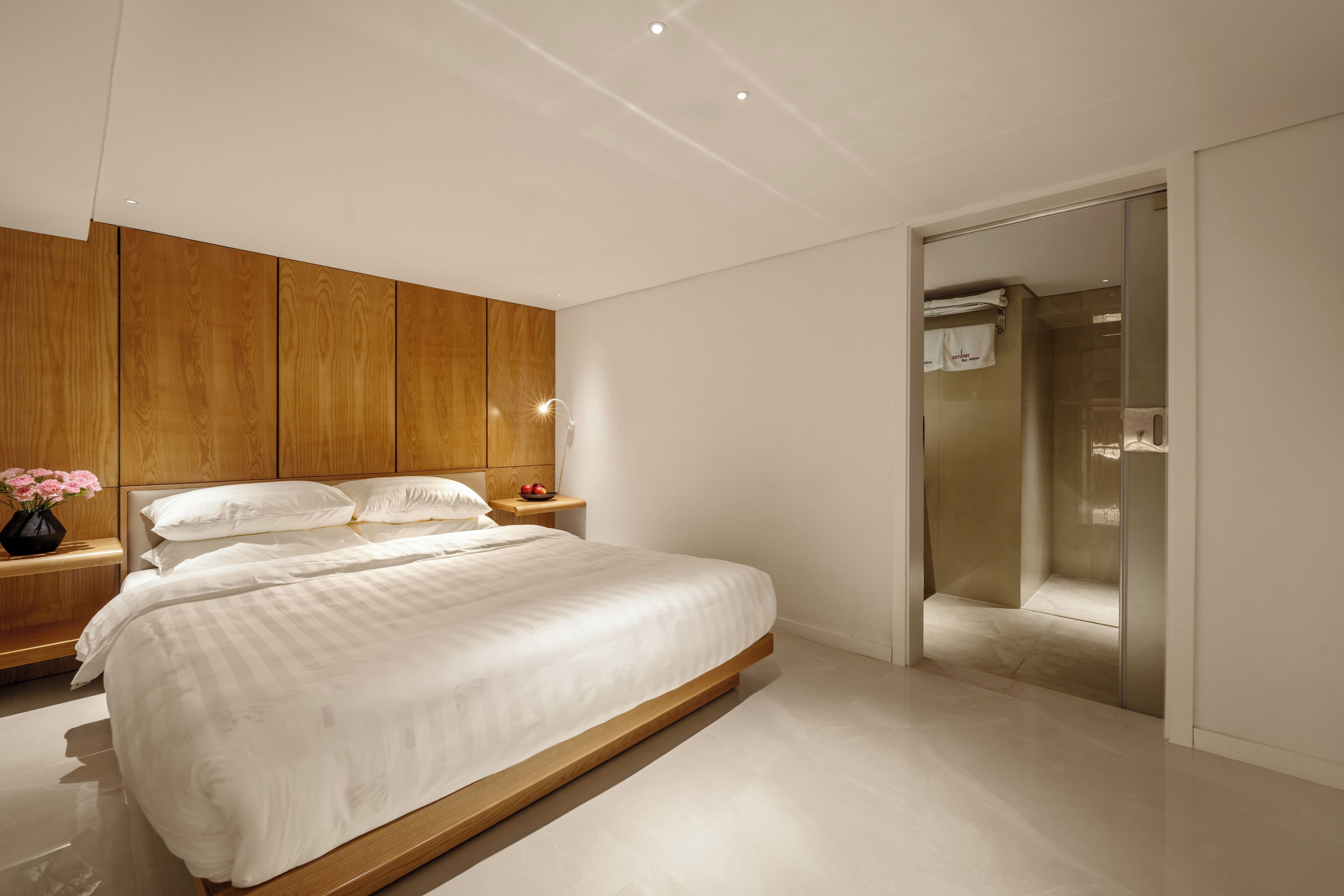 A modern bedroom with a large bed, wooden headboard, bedside tables, and a built-in wardrobe.