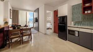 A modern kitchen with a dining area, a refrigerator, and a microwave. There is a view of a balcony through the window. - Amber Bay Hotel & Suites Da Nang (Da Nang)