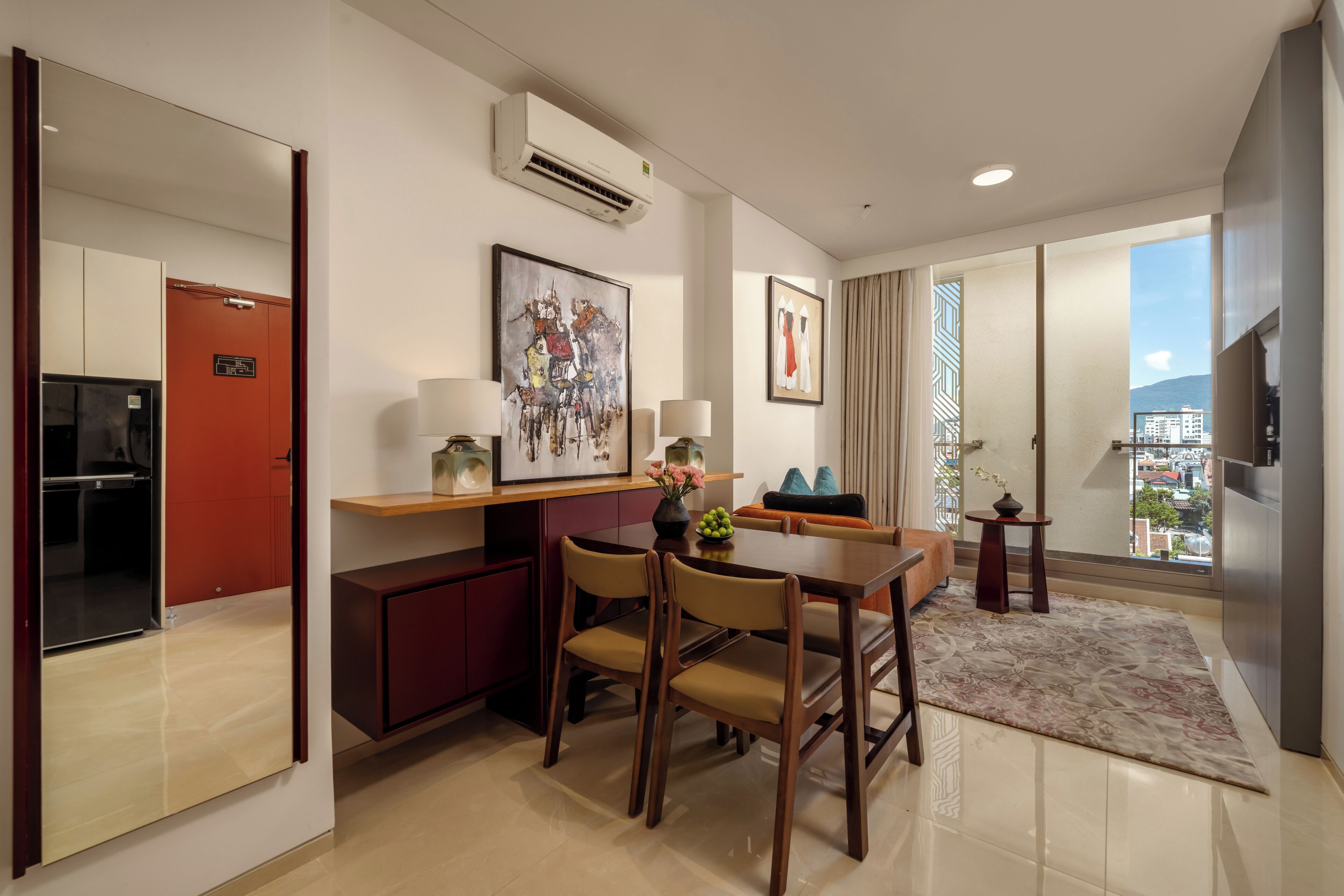 A modern hotel room with a dining area, a kitchen, and a balcony with a city view.