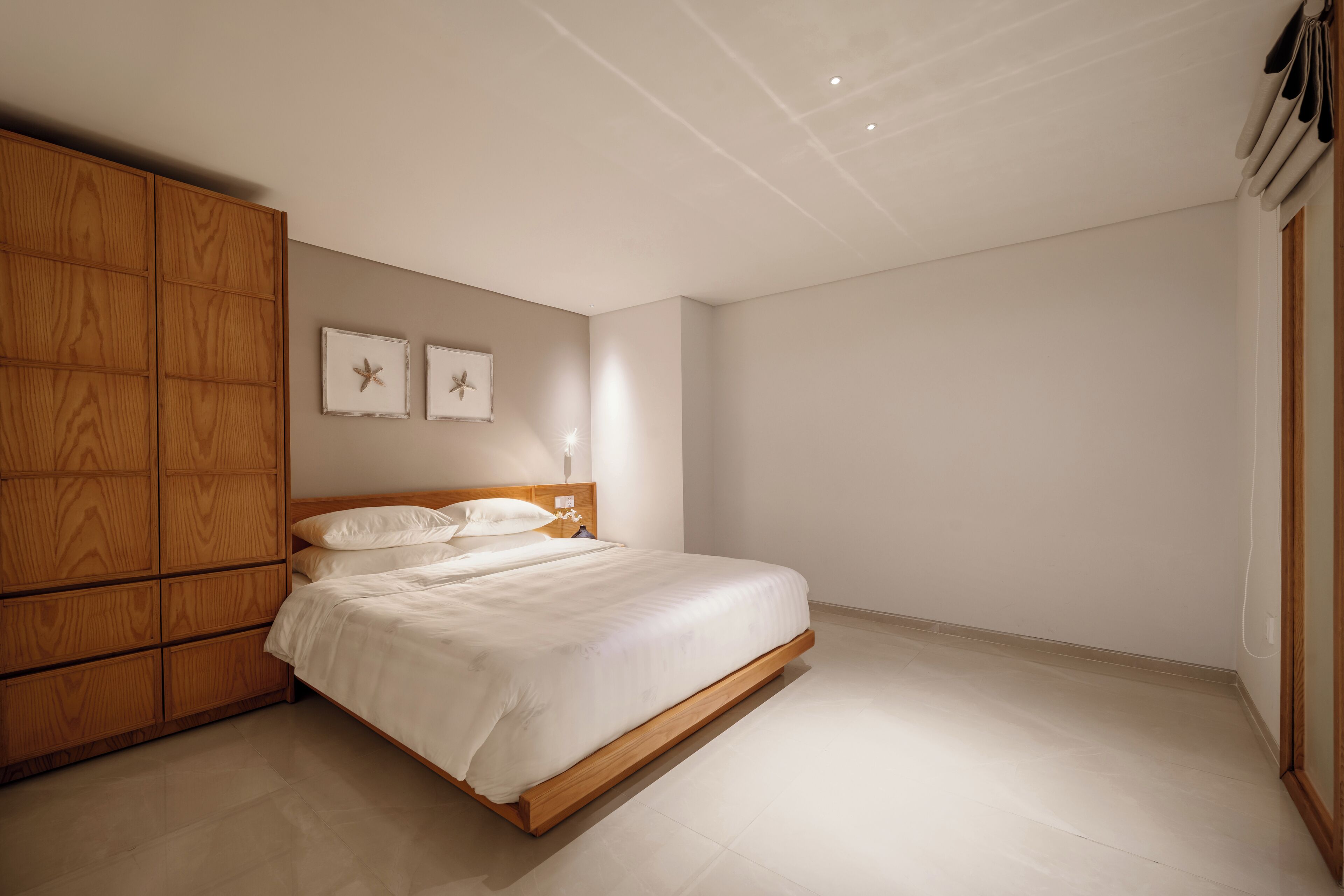 Ein Schlafzimmer mit einem Bettgestell aus Holz, weißer Bettwäsche und zwei Wandbildern mit Meeressternen.